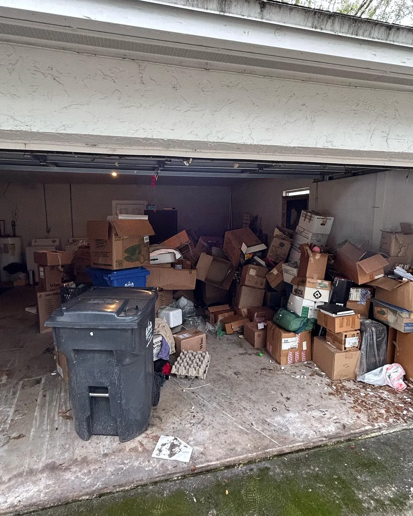 Before view of a heavily cluttered garage packed with boxes bins and various unwanted items prior to professional clearance service