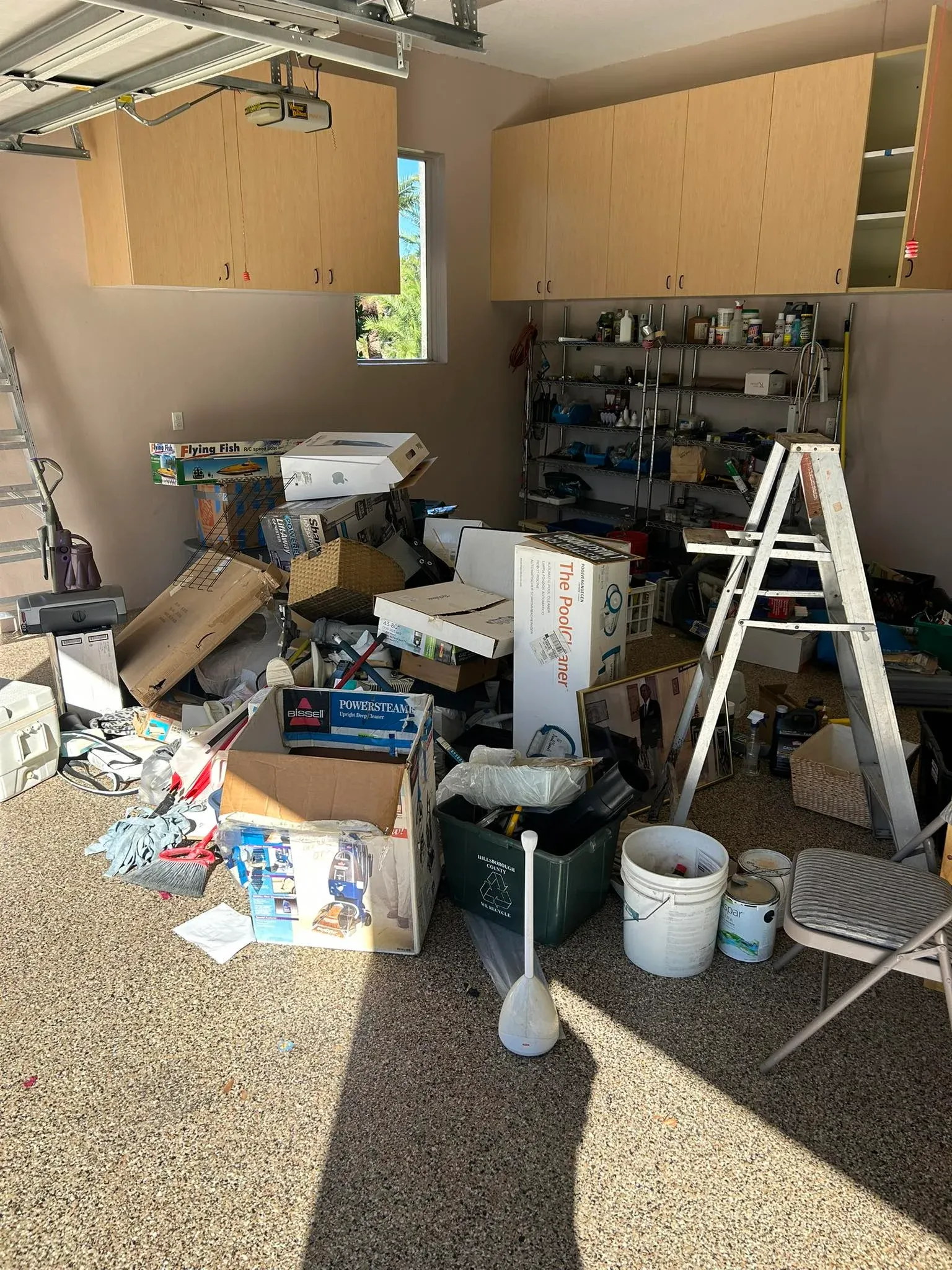 Before view of a cluttered patio and garage area filled with paint buckets ladders tools and debris prior to clearance