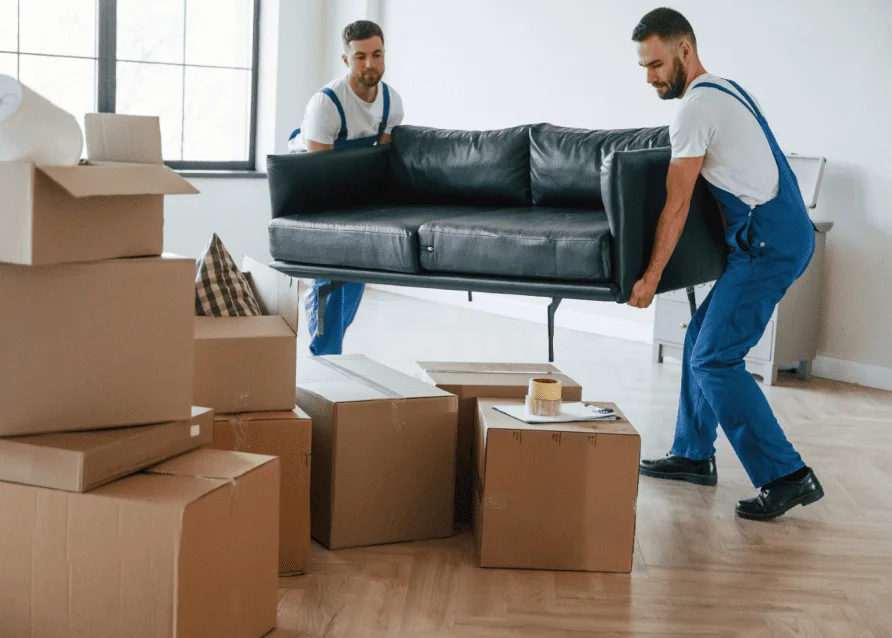 Two movers carrying a couch inside a home with boxes nearby