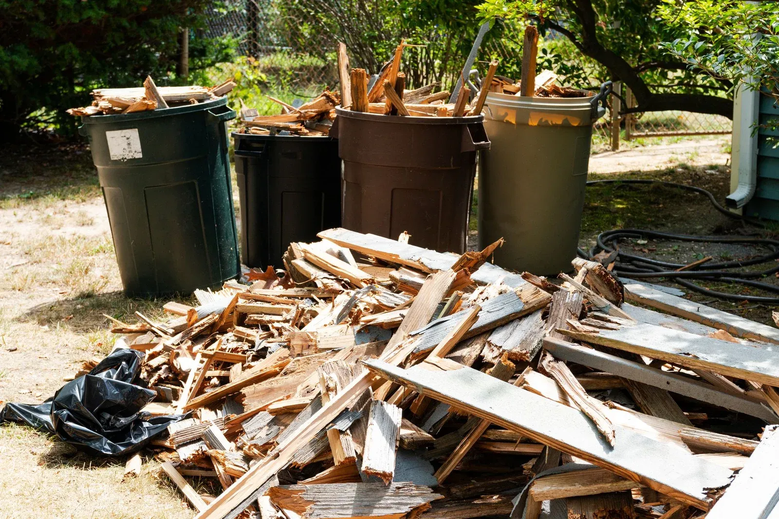 Large pile of broken wood timber and garden debris next to green wheelie bins outdoors