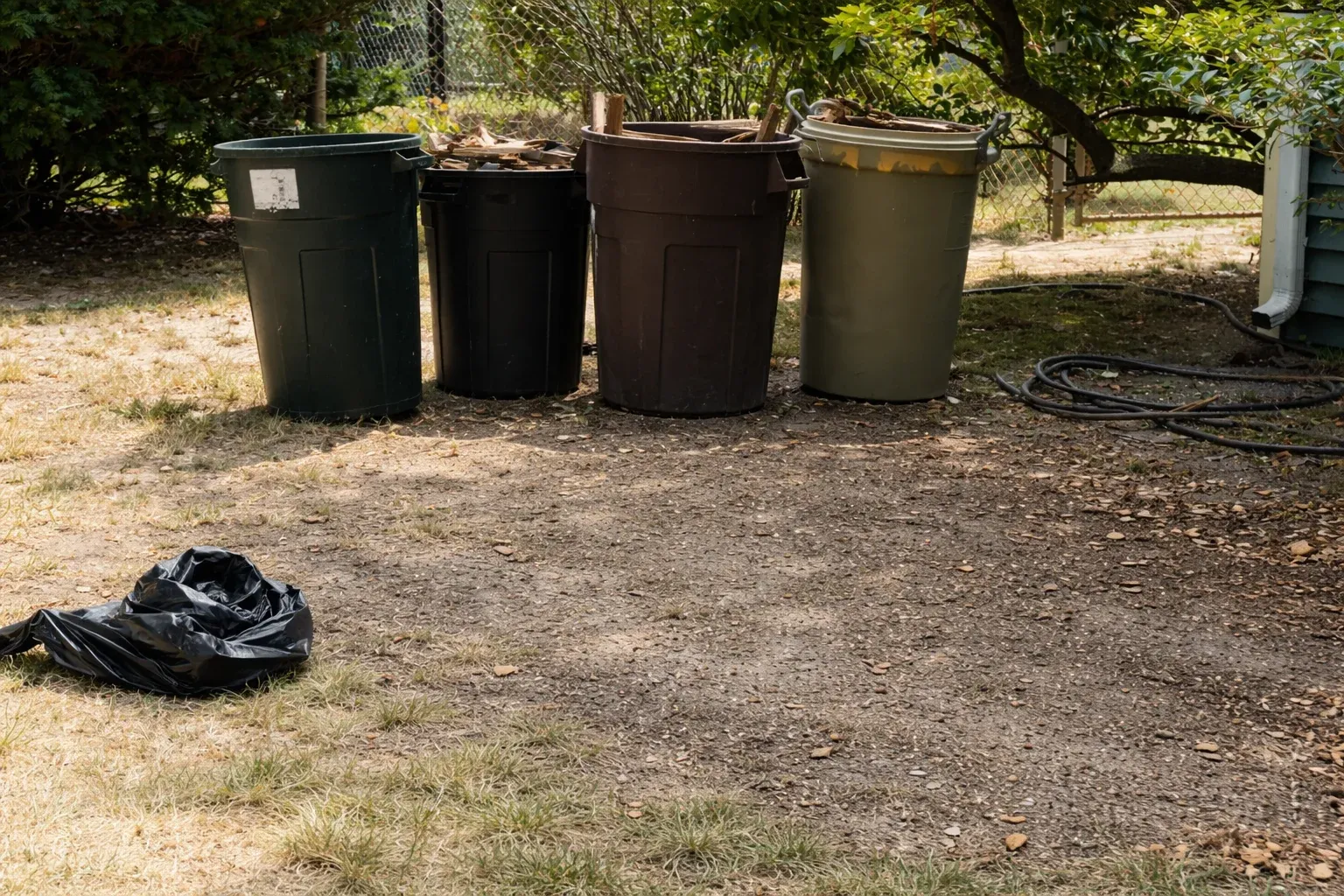 Three large green wheelie bins filled with garden waste placed outdoors on gravel